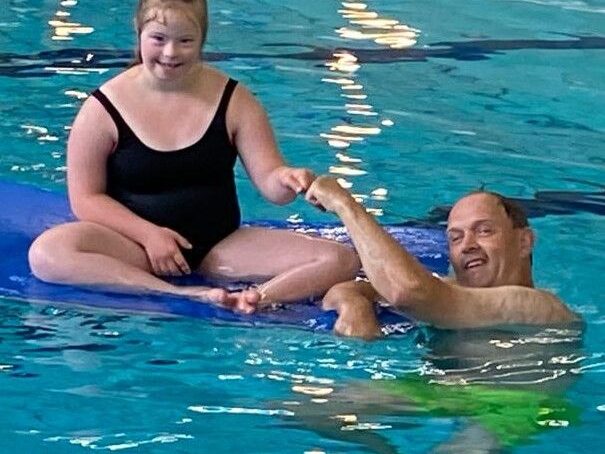 Zwemmer op een drijfmat met een begeleider in het water